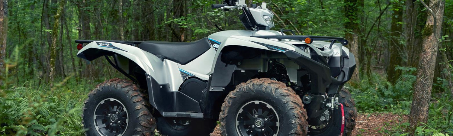 A white and black Yamaha® Grizzly® 700 ATV parked in the middle of a lush forest.